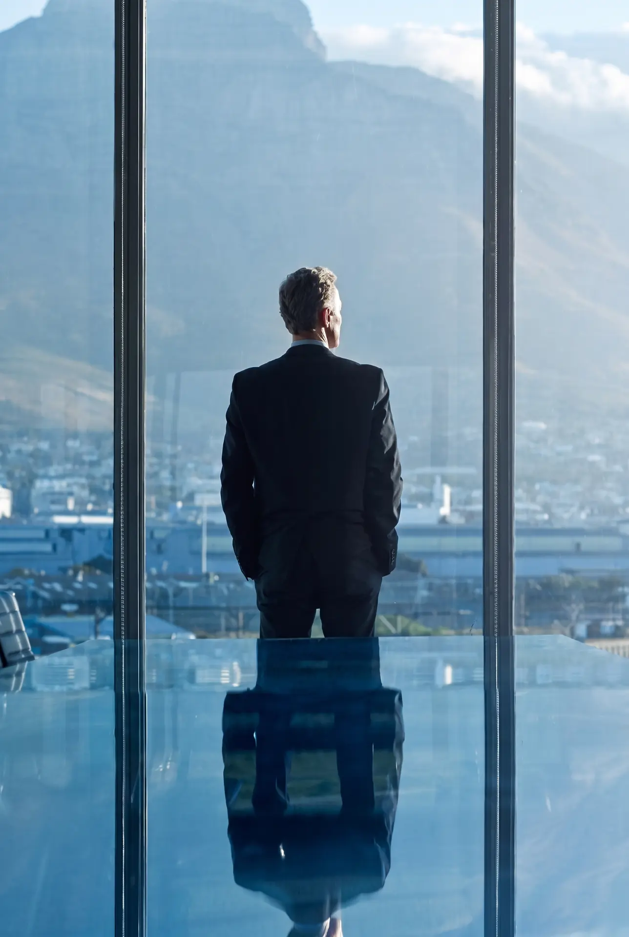 A man in a suit looking out over a mountain view through a glass window