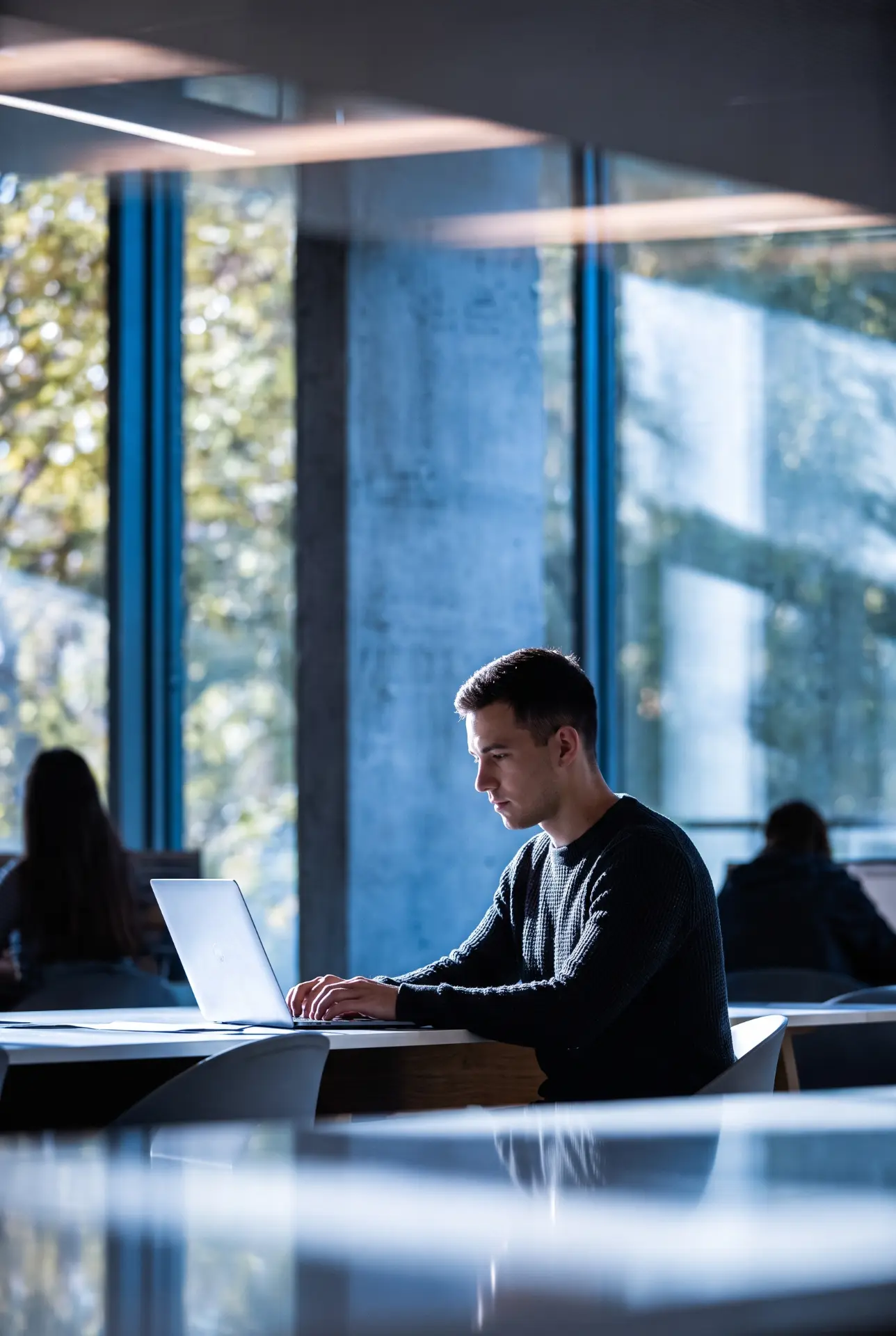 A man working on a laptop in a modern office with large windows